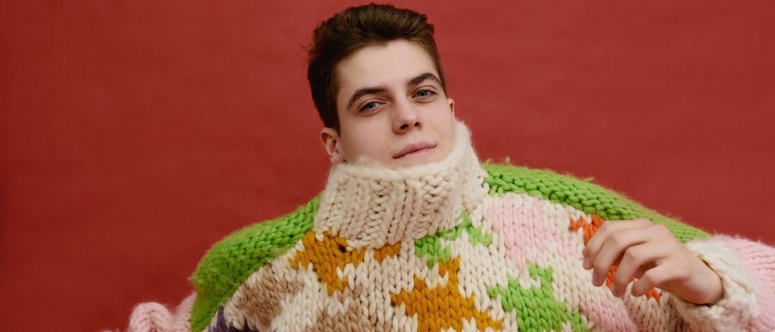 Young man wearing a hand-knitted multicoloured woollen jumper on a red background
