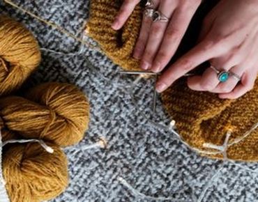 Mains en train de tricoter avec des pelotes de laine marron et des aiguilles