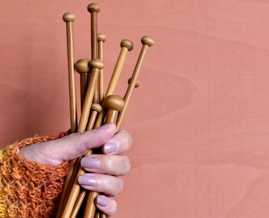 Hand holding several wooden knitting needles on a pink background