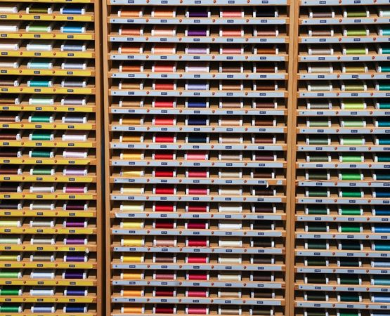 Mur organisé de bobines de fils multicolores rangées dans des compartiments.