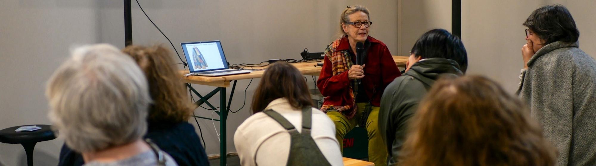 Speaker leading a workshop on patchwork before an audience, with a screen projecting a patchwork work.