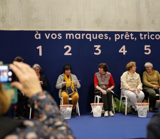 Participants knitting side by side on stage during the Speed Knitting competition at the Créations & Savoir-Faire show.