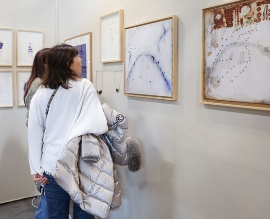 Visiteurs observant une exposition d’œuvres encadrées dans une galerie d’art, composée de photographies et créations textiles brodées au mur.