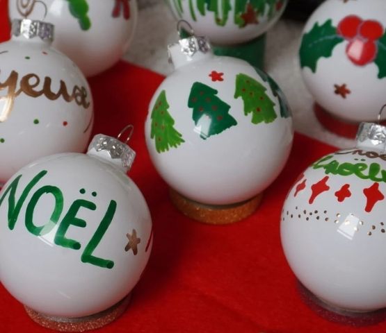 Boules de Noël blanches peintes à la main avec des motifs de sapins, de "Noël", et de décorations colorées