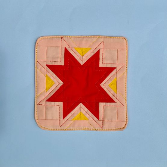 Patchwork square with red and yellow stars on a pink background.
