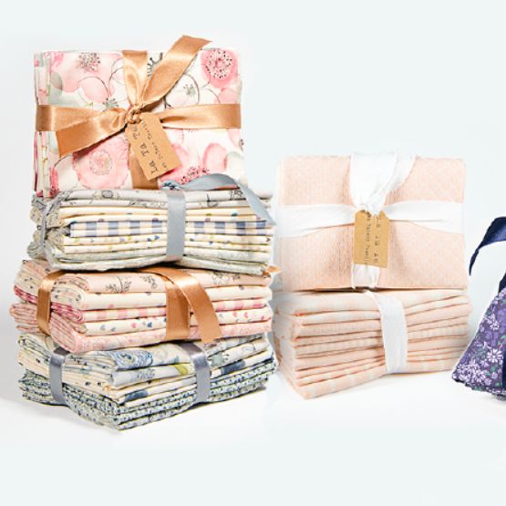 Stacks of folded fabrics in a variety of designs, tied with ribbons and kraft labels.
