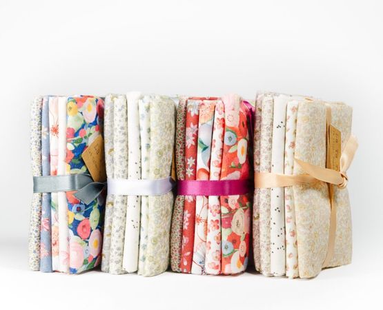 Piles de tissus pliés aux motifs variés, attachés avec des rubans et étiquettes kraft.