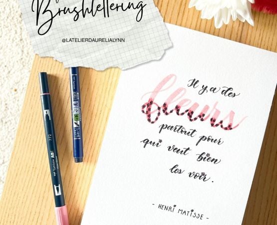 Feuille avec illustration calligraphiée "Il y a des fleurs partout pour qui veut bien les voir" et stylos pinceaux colorés.