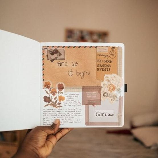 Main tenant un carnet de scrapbooking ouvert avec des éléments décoratifs.