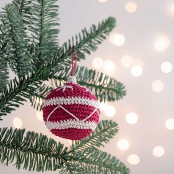Boule de Noël en maille crochetée suspendue à une branche de sapin.