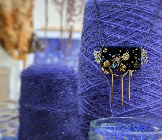 Collier artisanal noir décoré de perles dorées et argentées, présenté devant de grandes bobines de fil bleu