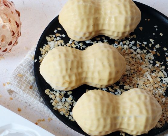 Confiseries en forme de cacahuète enrobées de chocolat blanc et disposées sur une assiette noire avec des éclats de biscuits.