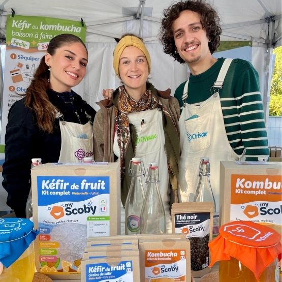 Three smiling people behind a stand displaying home-made kefir and kombucha kits from the My Scoby brand.