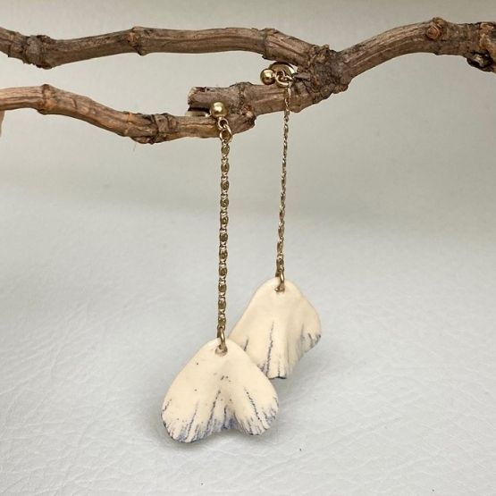 Pair of white ceramic pendant earrings hanging from a branch.