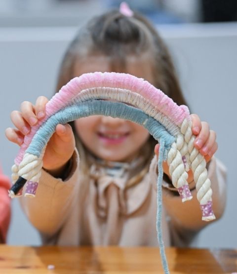 Enfant présentant une création en laine en forme d’arc-en-ciel lors d’un atelier créatif