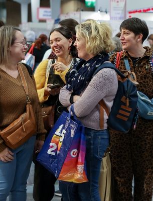Groupe de femmes échangeant et souriant lors d’un salon créatif avec sac shopping.