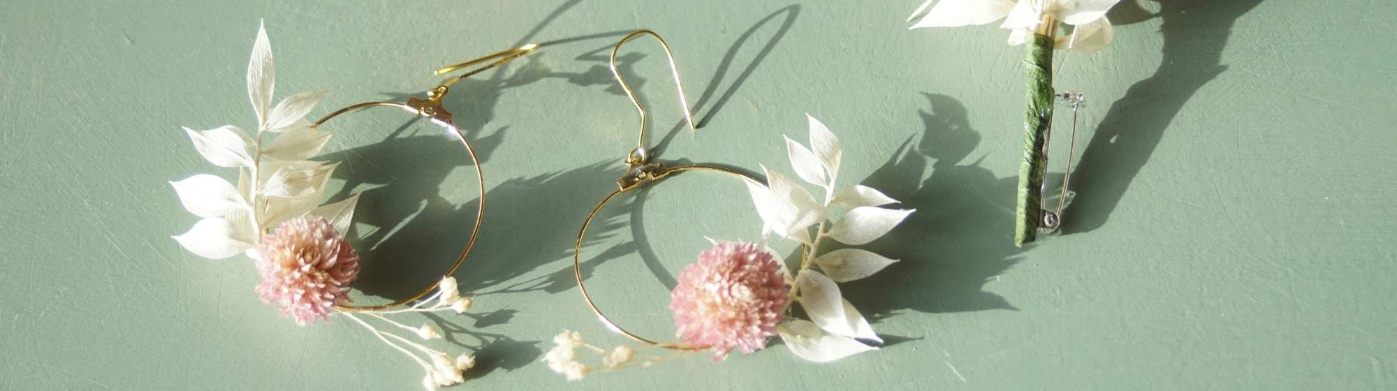 Vue panoramique de boucles d’oreilles et d’une boutonnière en fleurs séchées, posées sur un fond vert.