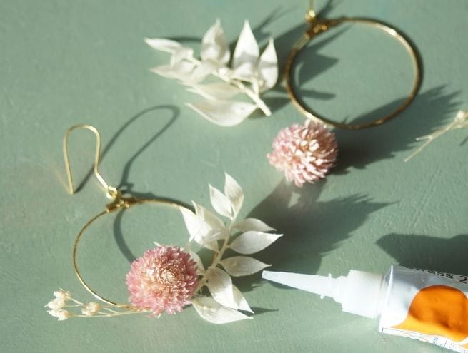 Étape d’assemblage des boucles avec fleurs et colle sur fond vert.