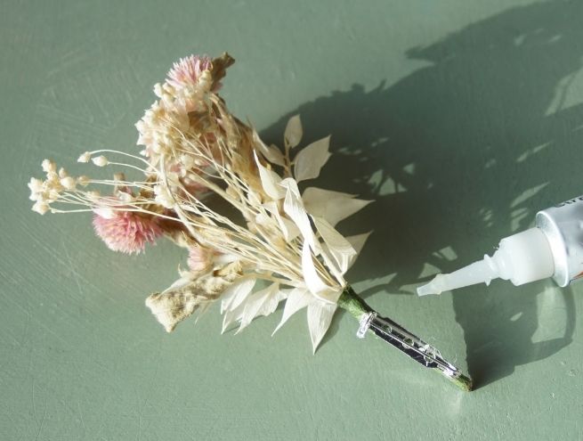 Dried flower buttonhole finished with a metal clip, next to a tube of glue.