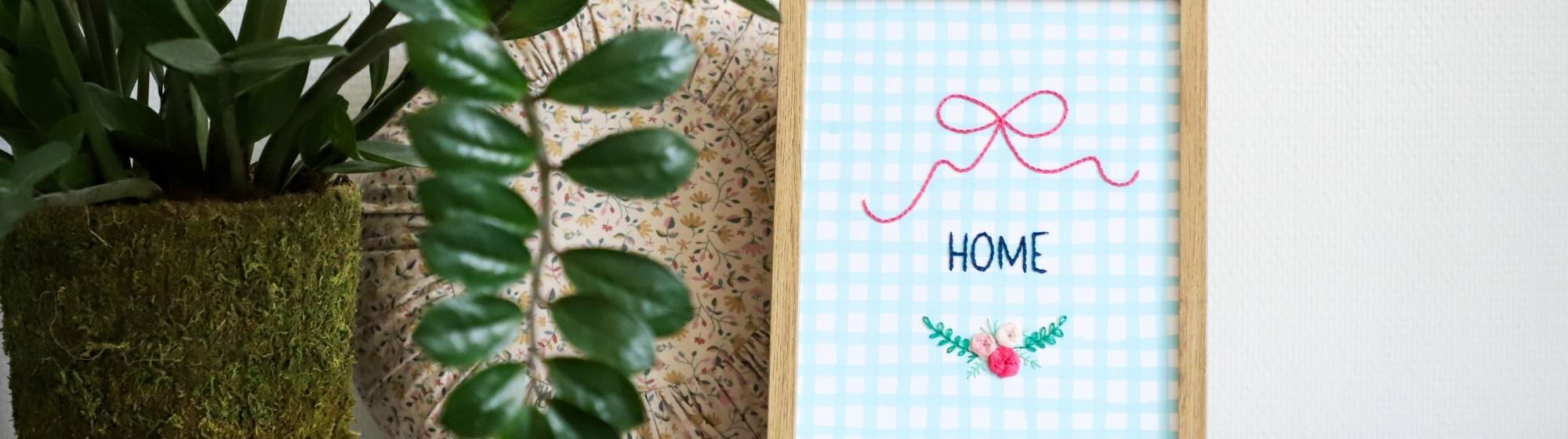 HOME decorative frame with embroidery on paper on a shelf with plants.