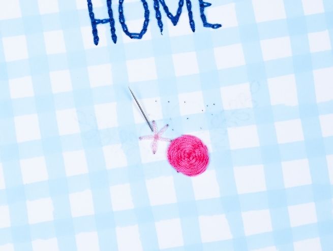 Make an embroidered star stitch around a pink circle on paper.