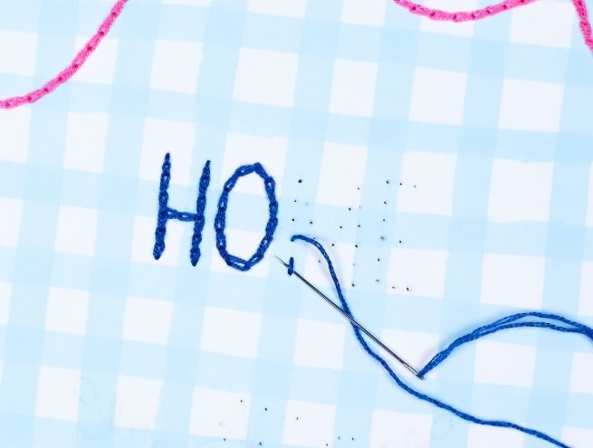 Detail of embroidery on paper with needle and blue thread on HOME motif.