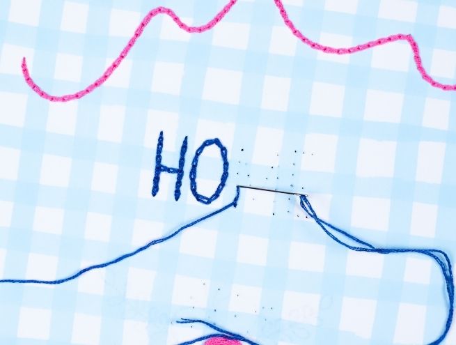 Embroidery on paper with blue thread forming the letters HO in progress.