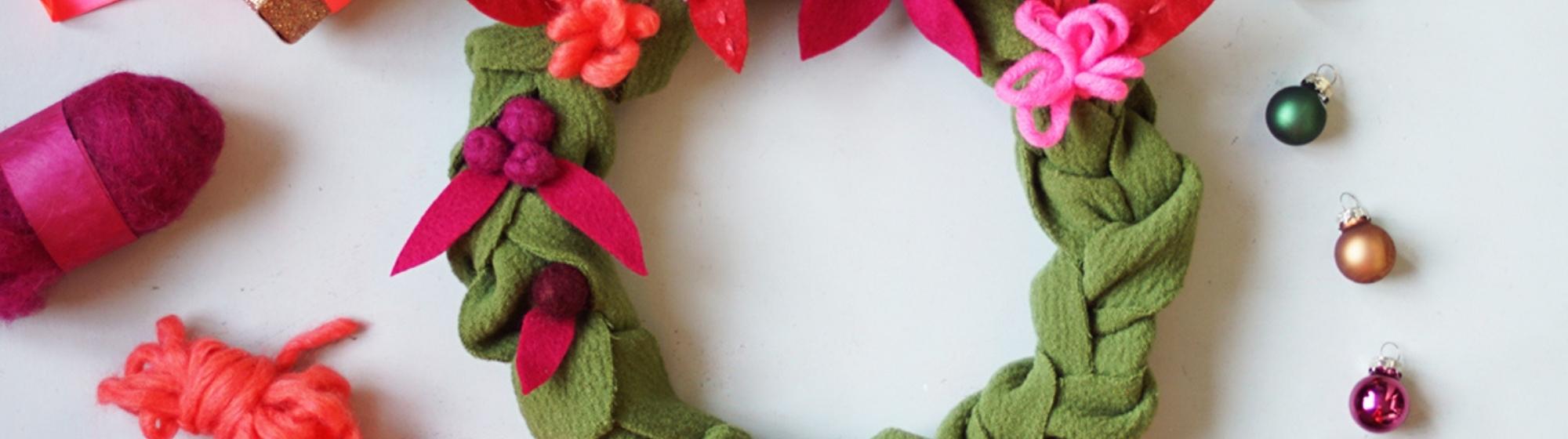 Couronne de Noël faite main avec des fleurs en feutre et des décorations en laine, accompagnée de petits cadeaux et d'ornements de Noël colorés.