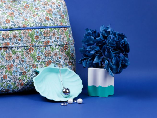Set the scene with a Jesmonite pot, a blue shell tray, jewellery and a floral bag.