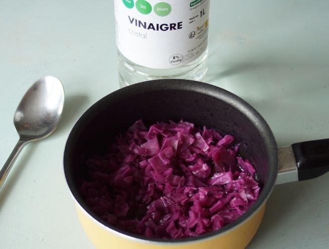 Purple cabbage cooked in a pan with a bottle of vinegar in the background.