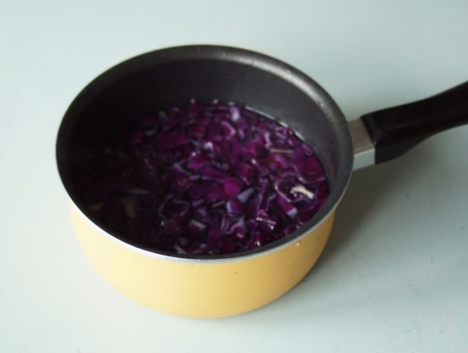 Chopped red cabbage in water at the bottom of a yellow pan.