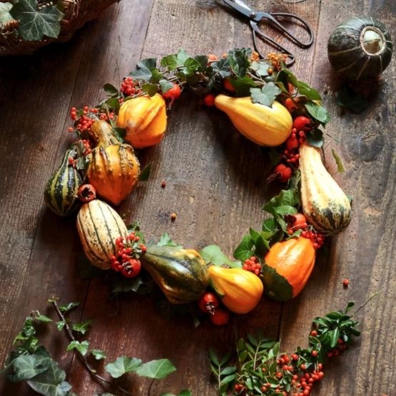 A decorative autumn wreath of mini pumpkins, red berries and green foliage.
