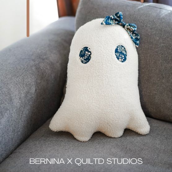 Ghost cushion in white fleece with blue bow, placed on a sofa.