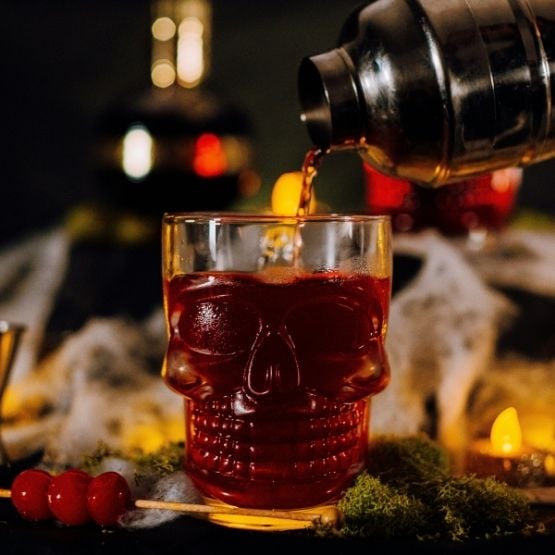 Cocktail rouge versé dans un verre en forme de crâne, décoré pour Halloween.