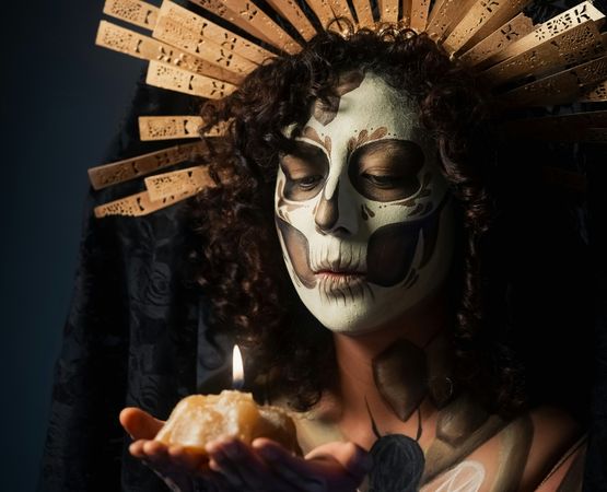 Personne maquillée en Catrina pour Halloween tenant une bougie dans une ambiance sombre