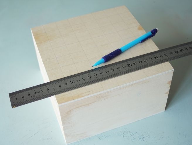 Boîte en bois avec une grille tracée au crayon pour préparer un plateau d’échecs