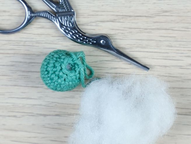 Cercle crocheté partiellement rembourré avec de la ouate synthétique, posé à côté de ciseaux de couture.