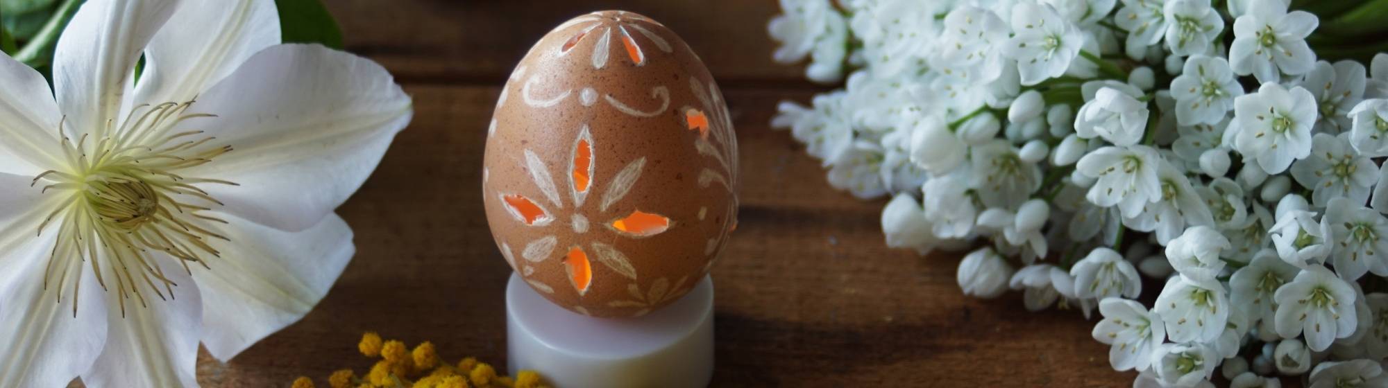 Œuf de Pâques décoré avec motifs gravés posé sur une table avec fleurs printanières.