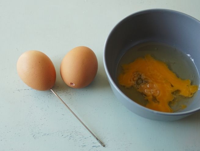 Vidage d’un œuf cru dans un bol après avoir percé la coquille pour un DIY de Pâques.