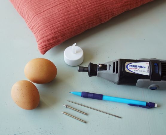 Matériel nécessaire pour graver un œuf de Pâques avec mini perceuse, œufs, bougie et outils de précision.