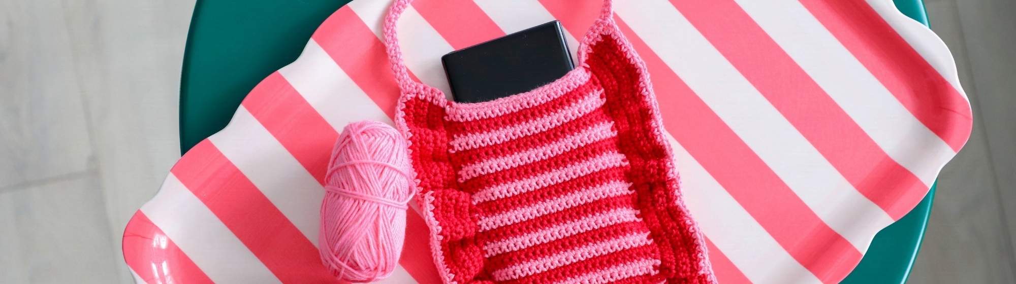 Pochette de téléphone en crochet rose et rouge réalisée avec du fil sur un tissu rayé