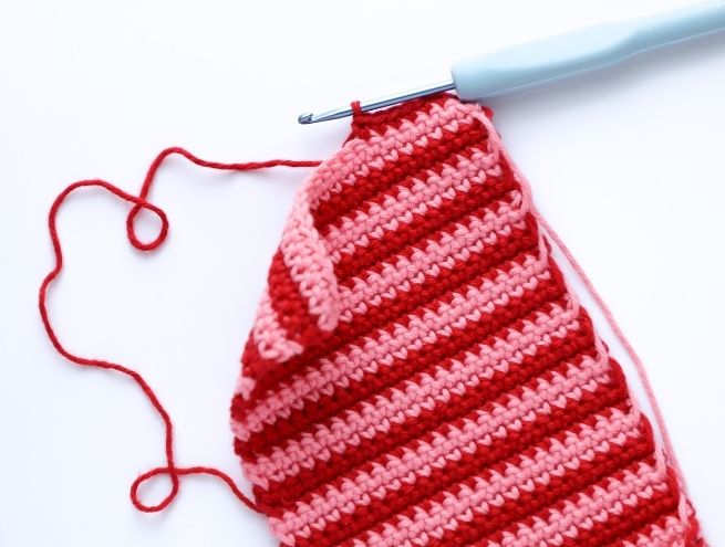 Étape avancée du crochet d’une pochette de téléphone rayée rose et rouge