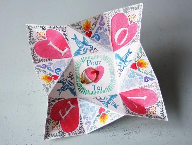 Puzzle en papier avec des motifs floraux et des cœurs, ouvert, avec une bague placée au centre.
