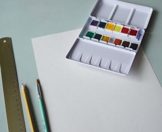 Page ouverte d'un carnet avec des dessins créatifs et des matériaux de bricolage comme des crayons, une règle et des pinceaux sur un fond en bois.