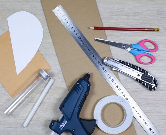 Materials needed to make a vase from recycled cardboard: scissors, ruler, cutter, hot glue and plastic bottle.