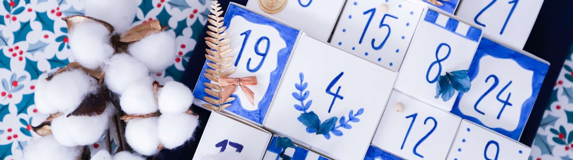 Calendrier de l’Avent fait main dans des tons bleus et blancs, décoré de fleurs séchées et chiffres peints.