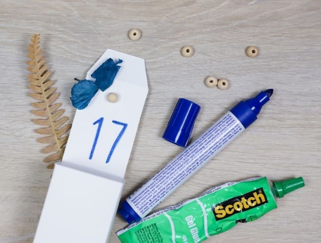 Décoration des boîtes du calendrier de l’Avent avec fleurs séchées et feutre bleu.