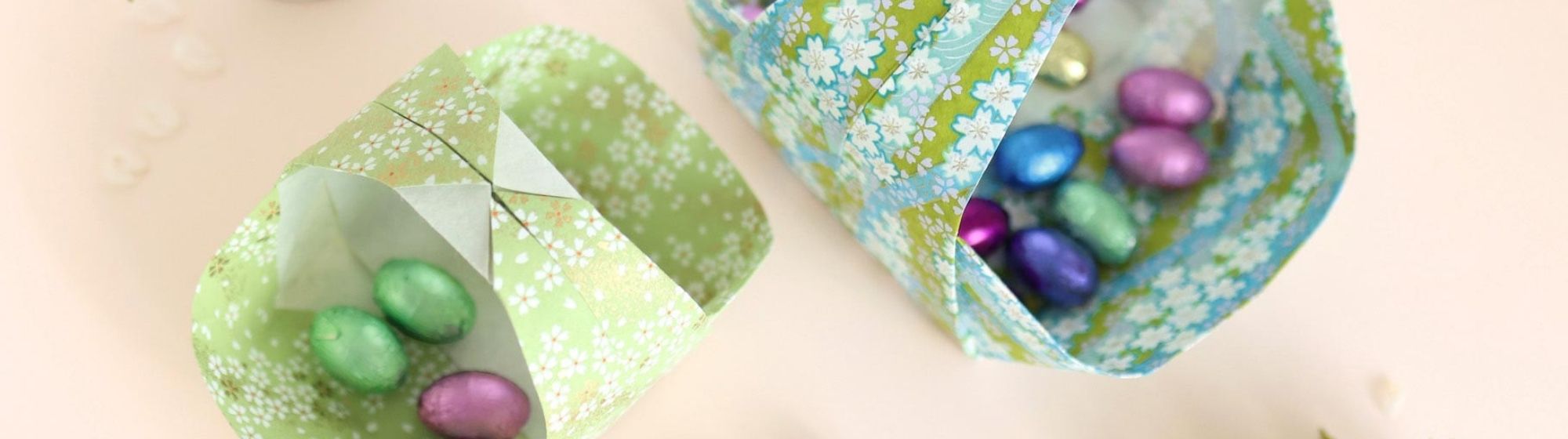 Paniers en origami remplis d’œufs de Pâques colorés avec papier à motifs floraux.