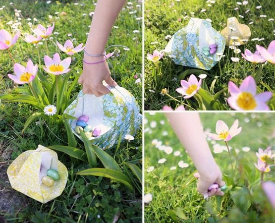 Paniers en origami remplis d’œufs de Pâques colorés disposés dans l’herbe et les fleurs printanières.
