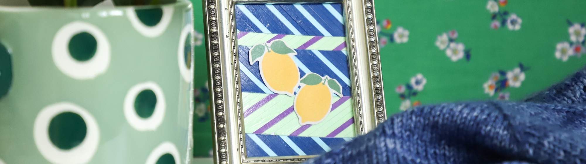 Small decorative frame with a lemon motif next to a plant in a colourful DIY world